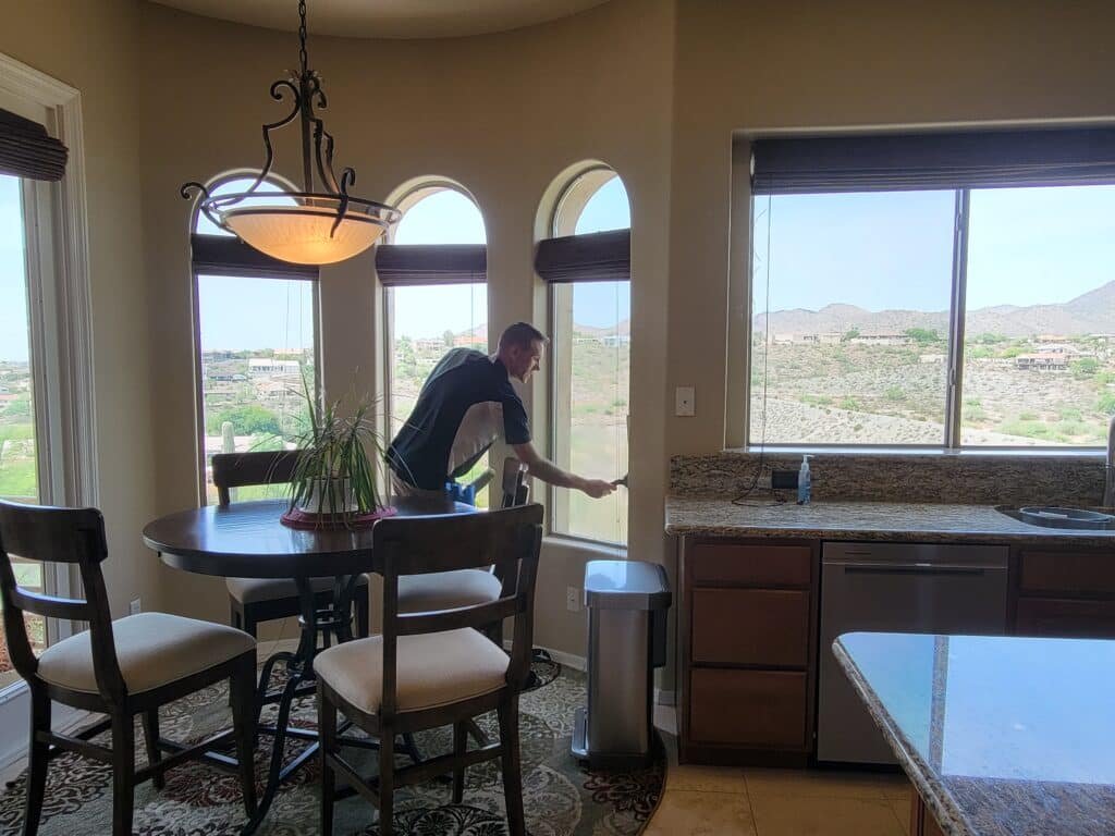 Image of Ace Window Cleanign expert cleaning a residential window. You can see the inside of a living room with large windows. In the center of the living room you can see the window cleanign expert at work.